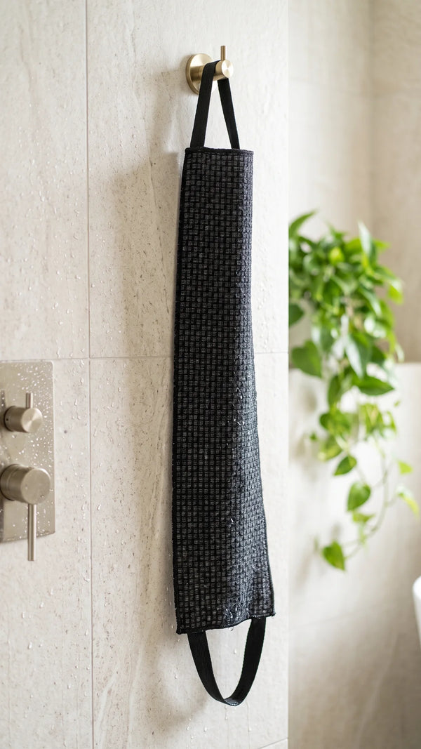 La serviette exfoliante noire Corpur suspendue par sa poignée dans la douche