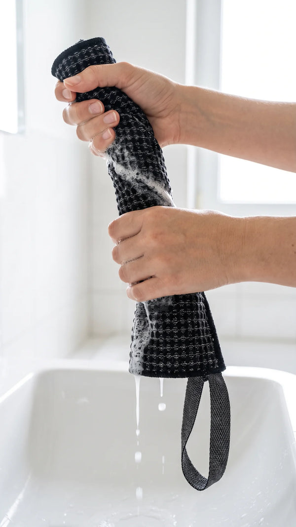 Mains qui essorent la serviette exfoliante noire Corpur pleine de mousse