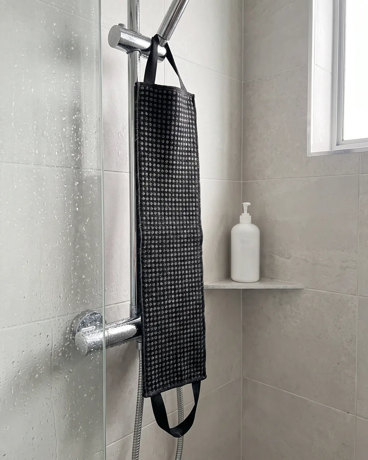 Photo d'exemple : serviette exfoliante noire suspendue par sa poignée à la barre de douche après la douche